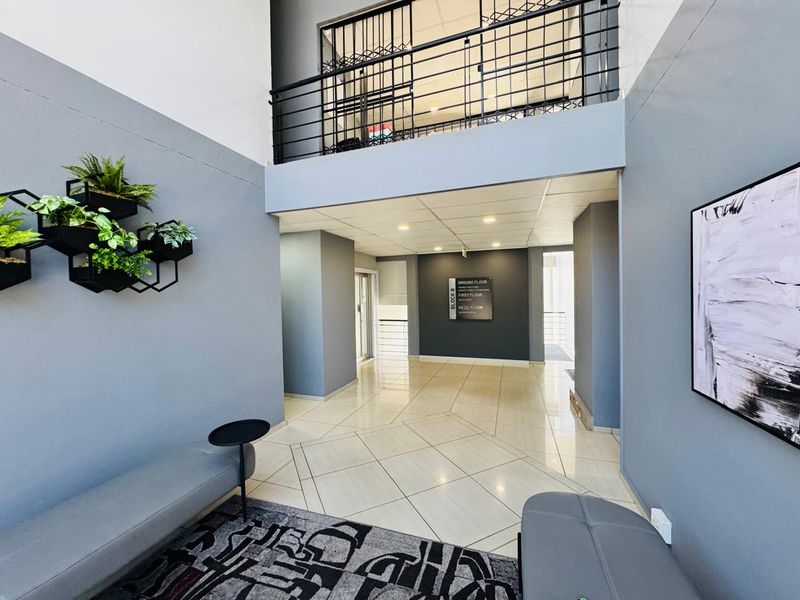 Modern office building entrance lobby featuring high ceilings, tiled flooring, and a mezzanine level with metal balustrades.