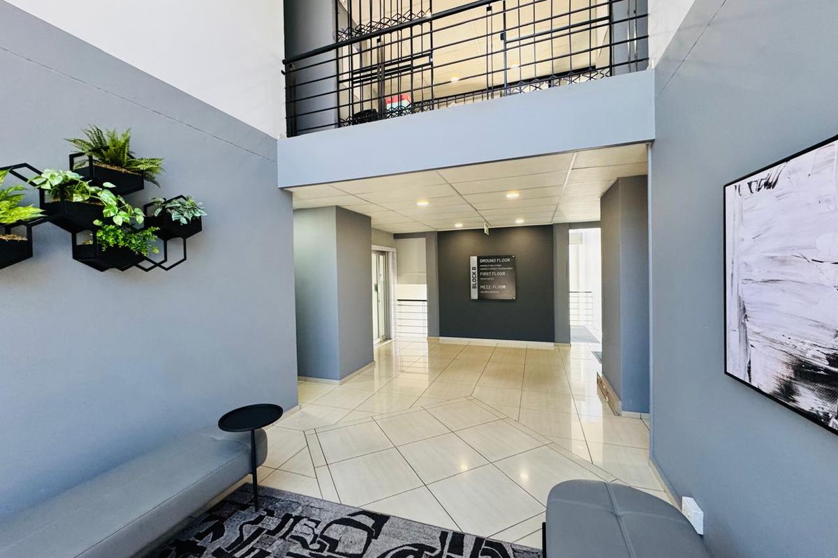 Modern office building entrance lobby featuring high ceilings, tiled flooring, and a mezzanine level with metal balustrades.