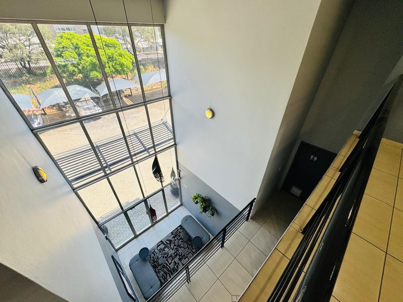 A bright, double-volume entrance foyer featuring expansive floor-to-ceiling windows, tiled flooring, and a modern metal staircase railing overlooking the ground floor.