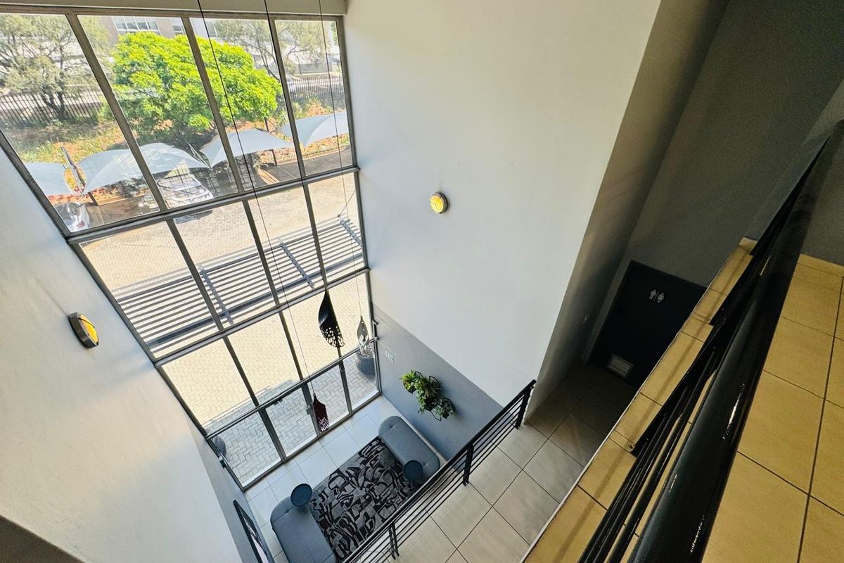 A bright, double-volume entrance foyer featuring expansive floor-to-ceiling windows, tiled flooring, and a modern metal staircase railing overlooking the ground floor.