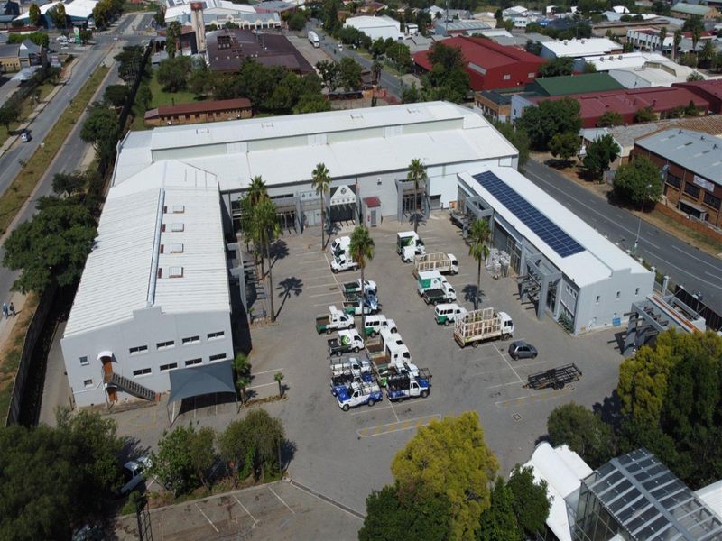 Aerial view of an industrial property featuring multiple warehouse buildings, extensive paved parking, and solar panel installations on the roof.