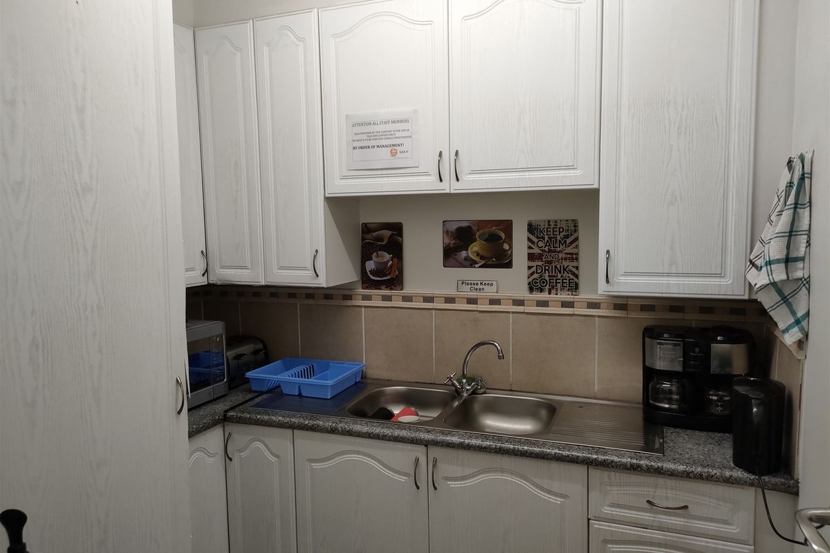 A compact kitchen area featuring white built-in cabinetry, a double bowl stainless steel sink, and granite countertops with a tiled backsplash.