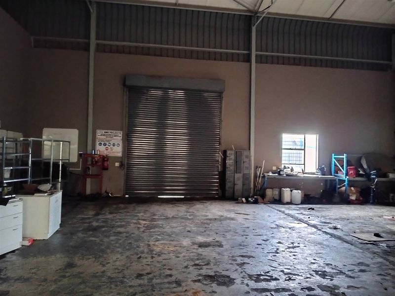 Spacious industrial utility area featuring high ceilings, a large roller shutter door, and durable concrete flooring, suitable for storage or workshop operations.
