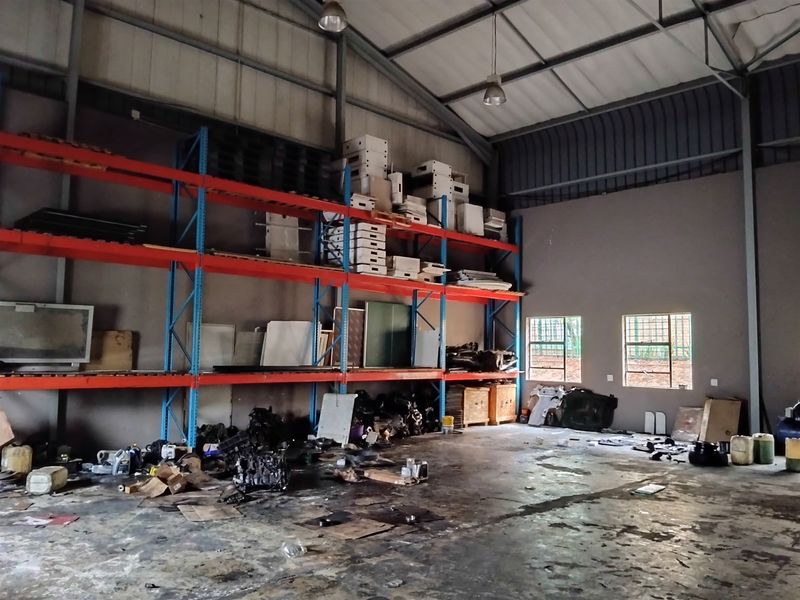 Spacious industrial utility area featuring high ceilings, exposed steel trusses, heavy-duty racking systems, and durable concrete flooring suitable for storage or workshop use.
