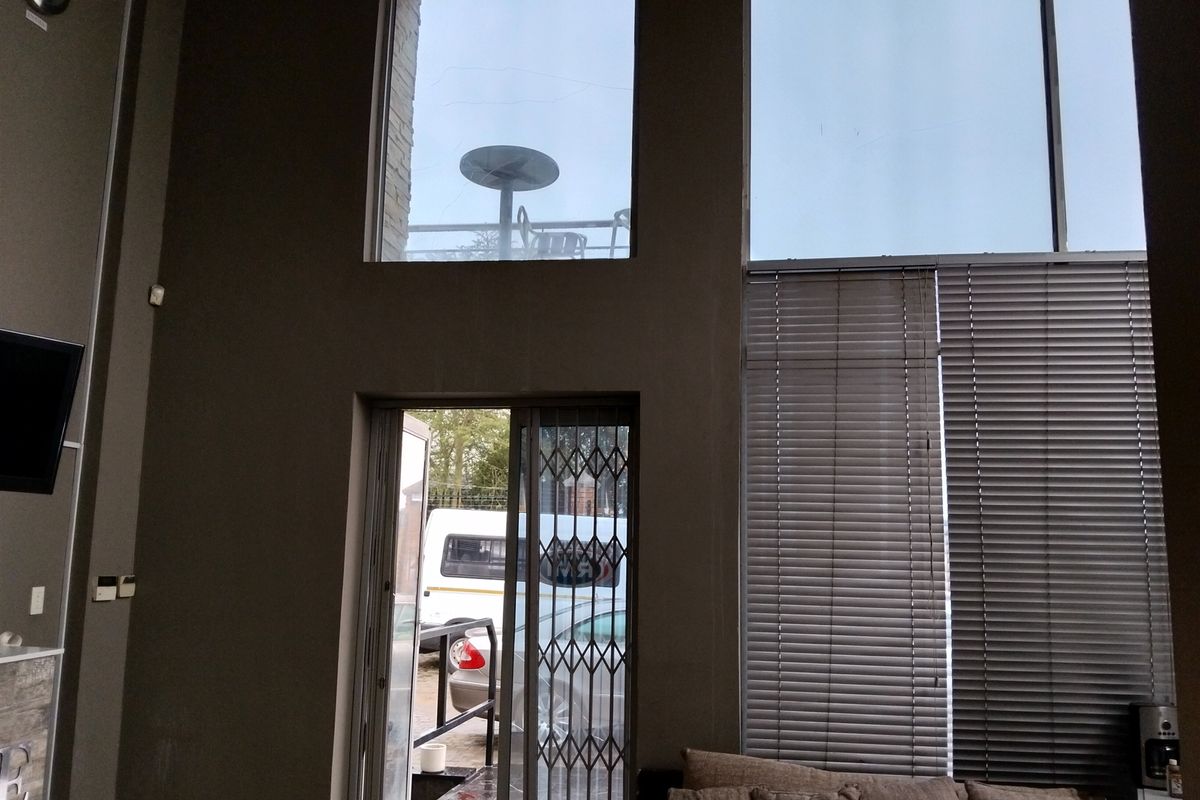 Spacious living area featuring double-volume windows, natural light, and a sliding door with security gate access to the exterior.