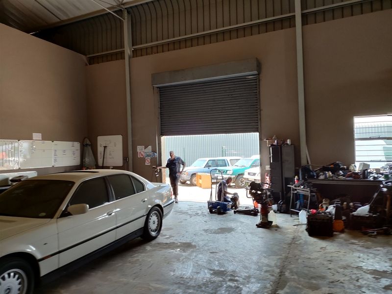 Spacious industrial garage featuring high ceilings, a large roller shutter door, and durable concrete flooring, suitable for workshop or storage use.