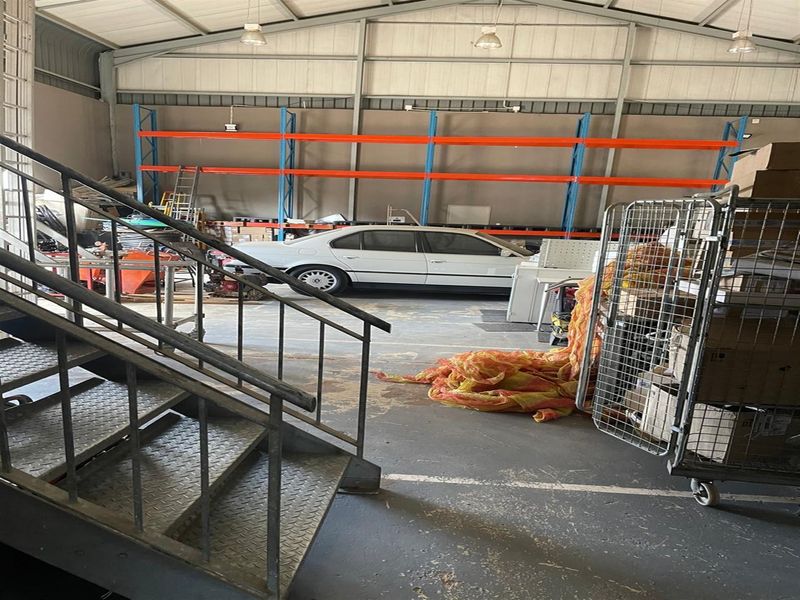 Industrial warehouse space featuring high ceilings, exposed steel roof structure, heavy-duty metal staircase, and integrated industrial racking systems.