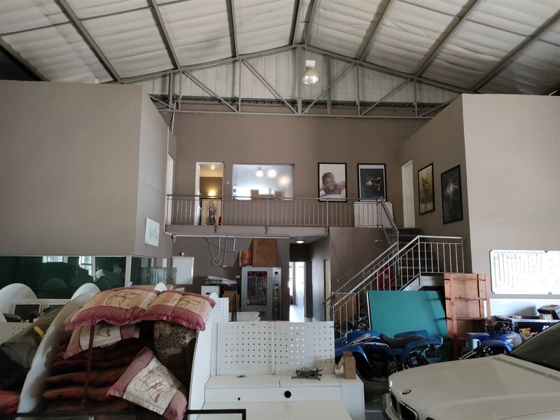 Spacious industrial utility area featuring a mezzanine level with metal staircase, high exposed roof trusses, and functional open-plan layout suitable for various commercial uses.