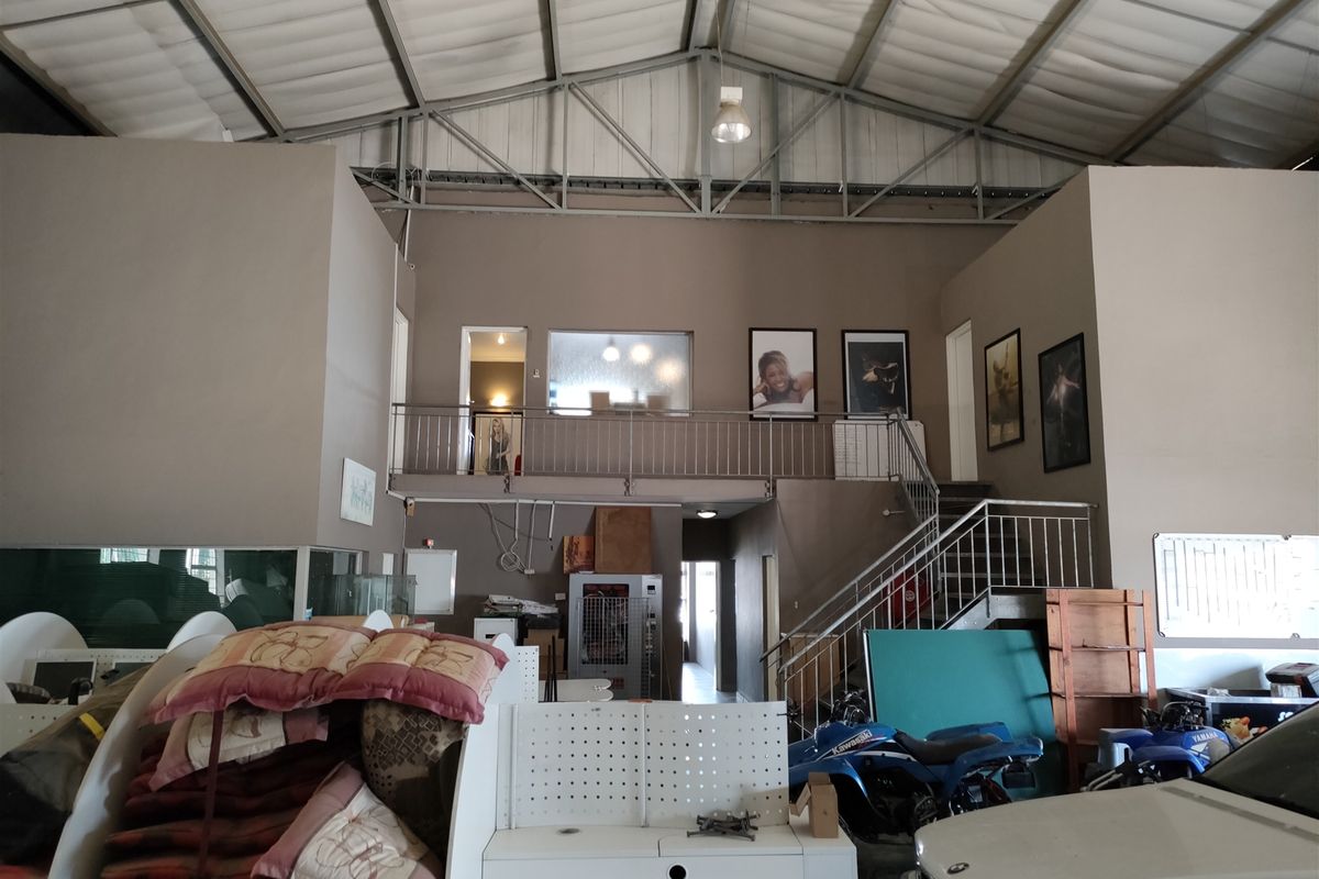 Spacious industrial utility area featuring a mezzanine level with metal staircase, high exposed roof trusses, and functional open-plan layout suitable for various commercial uses.