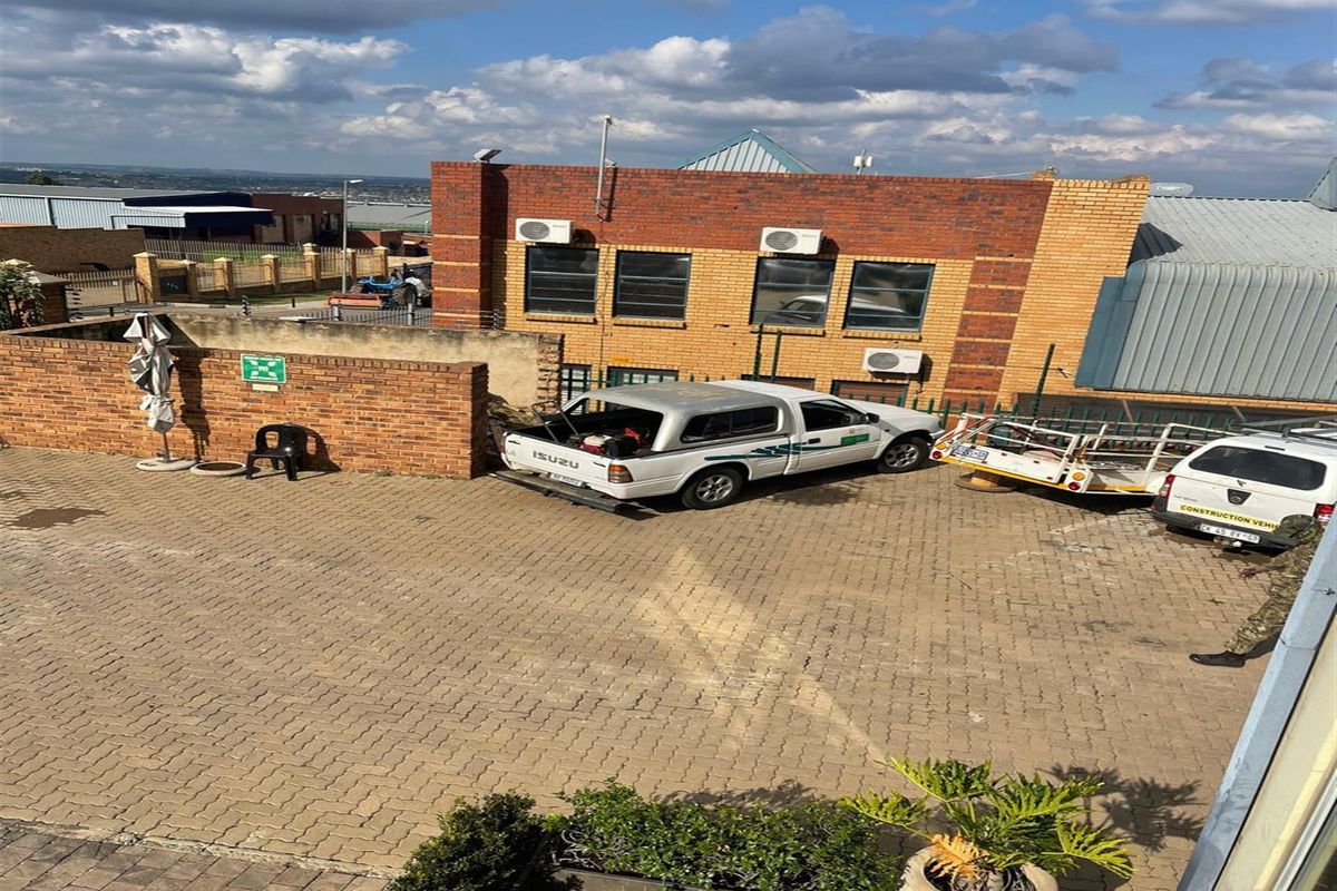 An elevated view of a paved industrial yard featuring a face brick building facade with multiple wall-mounted air conditioning units and perimeter security fencing.