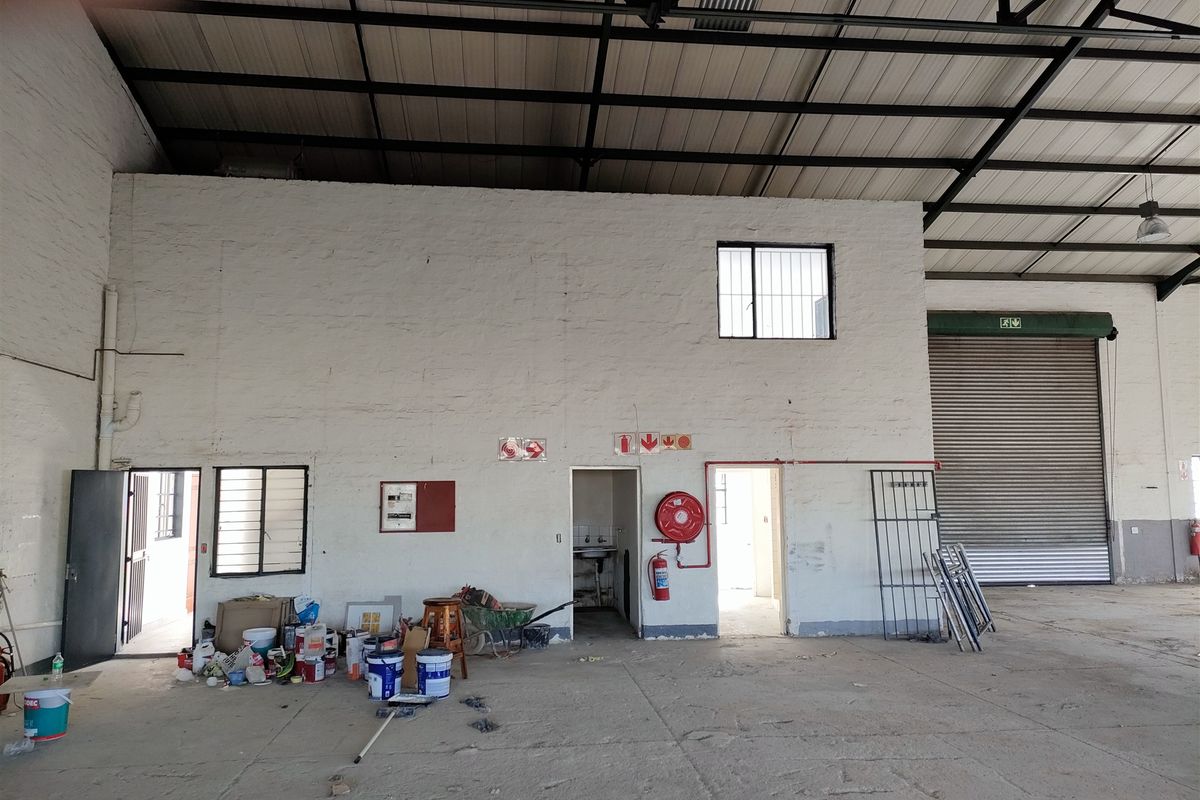 Spacious industrial utility area featuring high exposed steel roof trusses, concrete flooring, and a large roller shutter door for easy access.