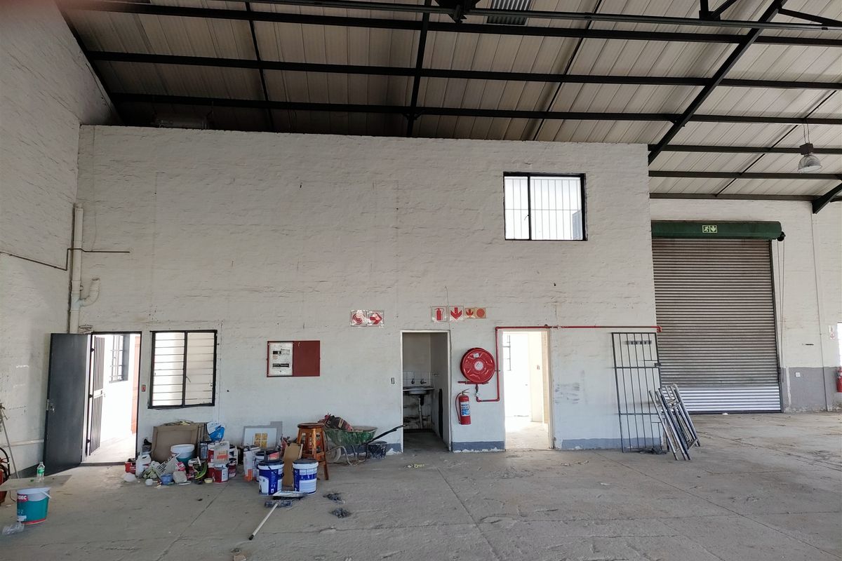 Spacious industrial warehouse area featuring high exposed steel roof trusses, a large roller shutter door, and integrated fire safety equipment.