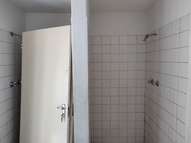 A functional industrial-style communal shower area featuring tiled walls and basic shower fixtures, currently in need of cosmetic updates.