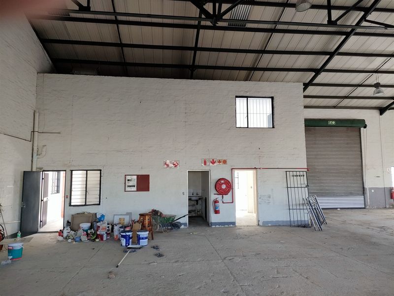 Spacious industrial utility area featuring high exposed steel roof trusses, concrete flooring, and a large roller shutter door for easy access.