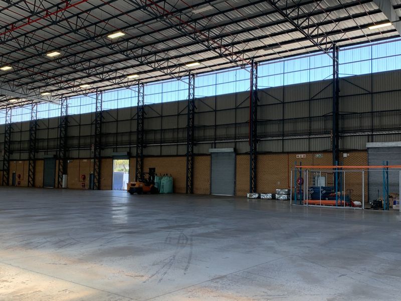 Spacious industrial warehouse featuring high ceilings with exposed steel trusses, concrete flooring, and multiple roller shutter doors for efficient logistics and storage operations.