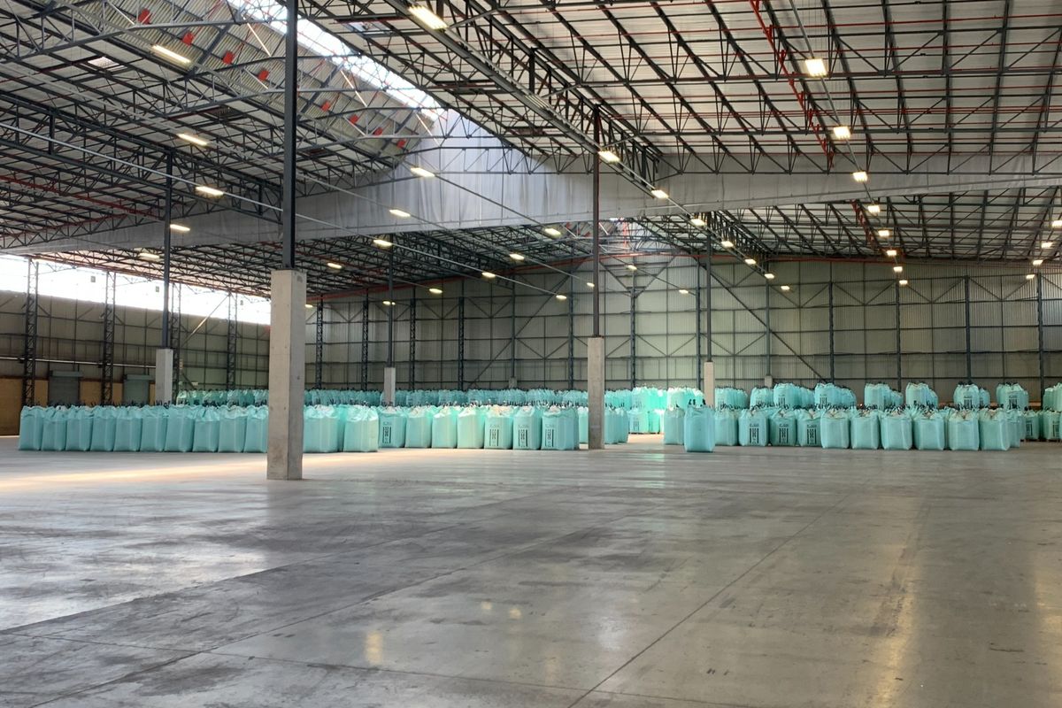 Spacious industrial warehouse featuring high-clearance exposed steel truss roofing, polished concrete flooring, and extensive overhead lighting, currently utilized for bulk storage.