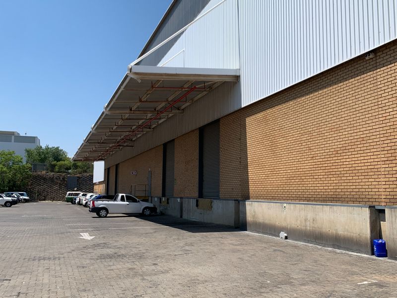 Industrial warehouse exterior featuring a paved loading yard, concrete loading docks, roller shutter doors, and a protective canopy over the loading area.