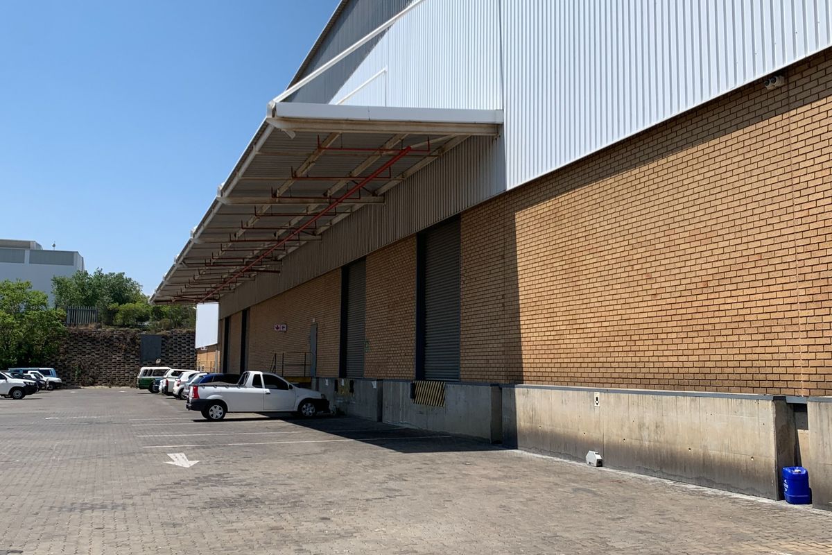 Industrial warehouse exterior featuring a paved loading yard, concrete loading docks, roller shutter doors, and a protective canopy over the loading area.
