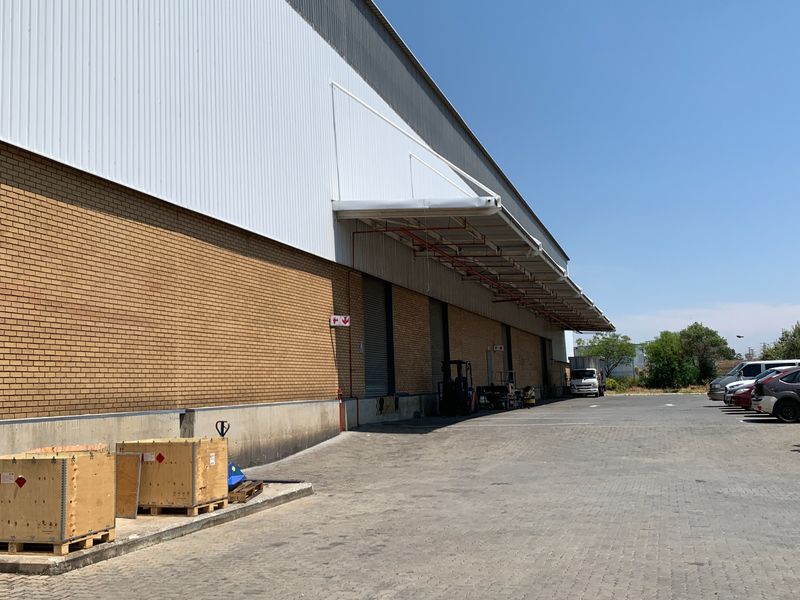 Industrial warehouse exterior featuring a brick and metal facade, loading canopy, roller shutter doors, and a spacious paved yard area.