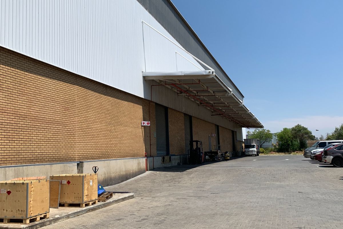 Industrial warehouse exterior featuring a brick and metal facade, loading canopy, roller shutter doors, and a spacious paved yard area.