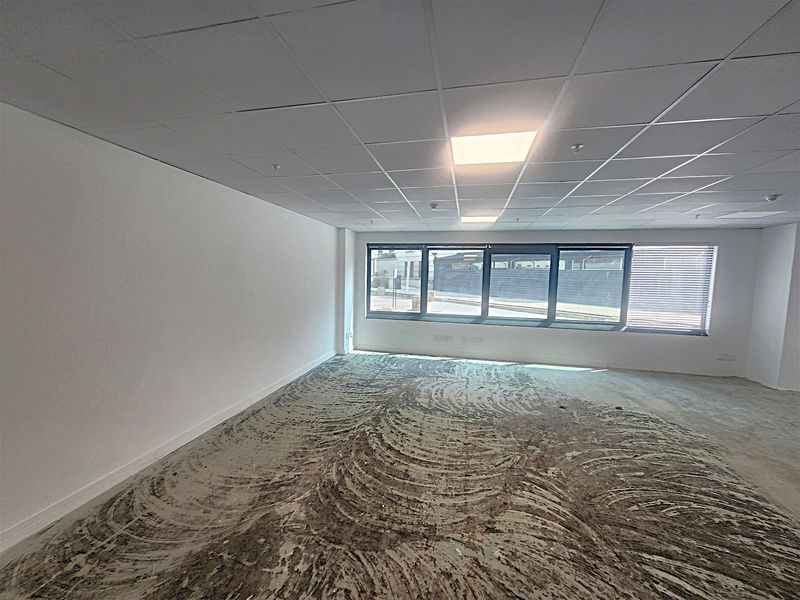 An empty office space featuring a suspended ceiling, recessed lighting, and large windows with blinds, currently requiring new flooring installation.