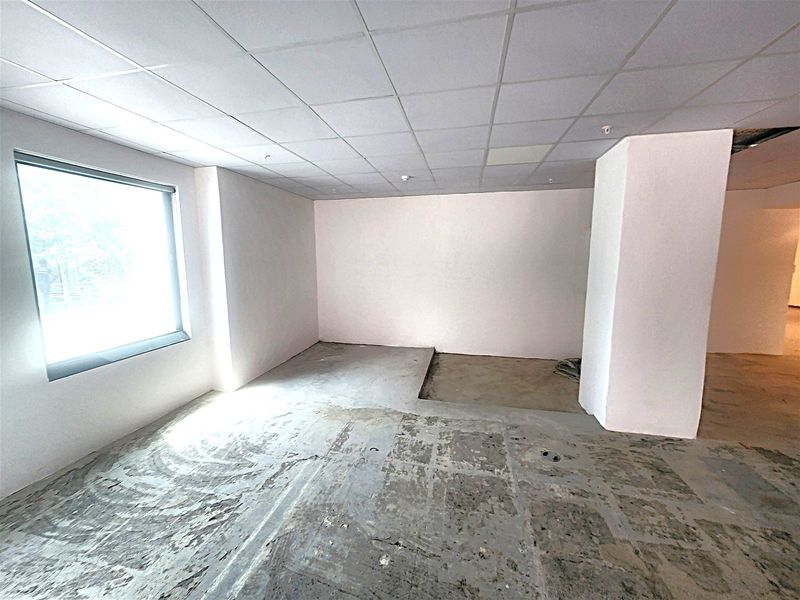 An empty office space featuring a suspended ceiling, large window, and unfinished concrete flooring, ready for renovation or custom fit-out.