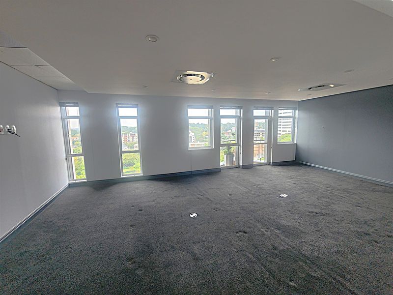A spacious, empty office area featuring large windows with natural light, recessed ceiling lighting, and integrated floor power outlets.