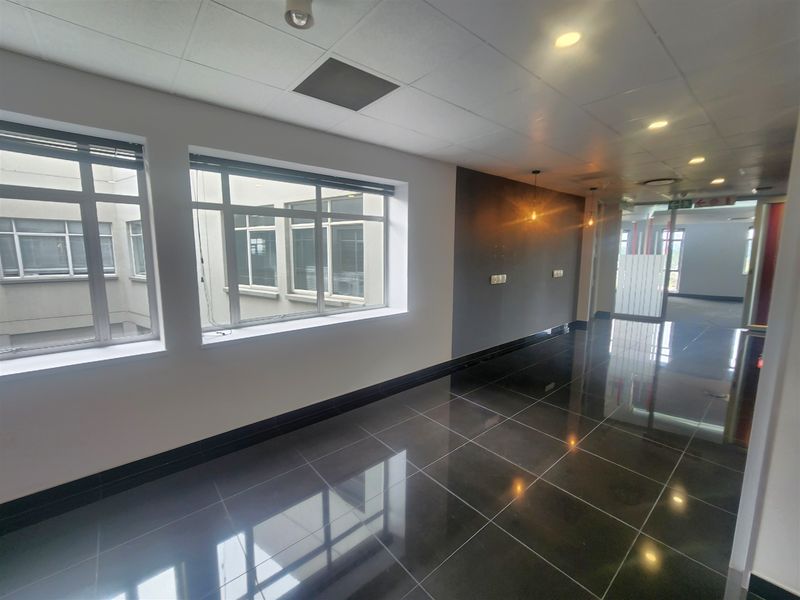 A bright, modern office space featuring polished dark floor tiles, large windows providing natural light, and a clean, professional finish throughout.