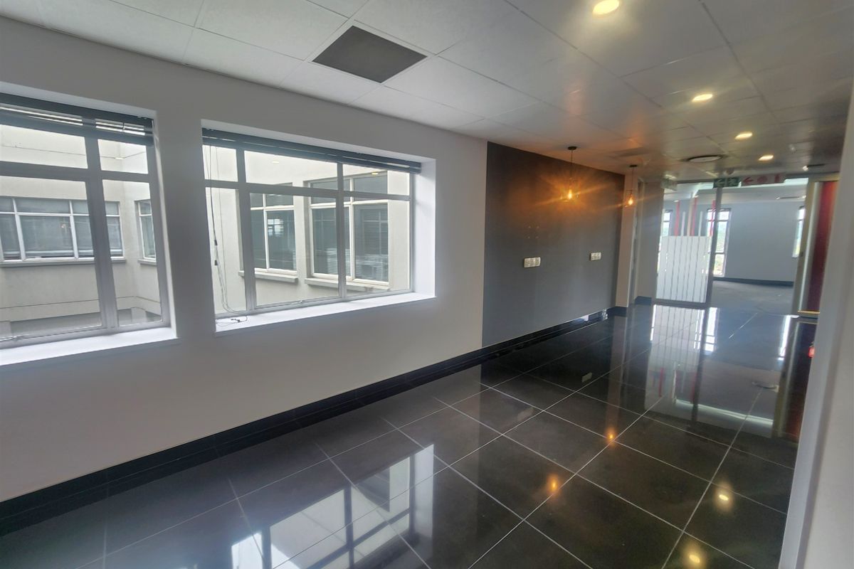 A bright, modern office space featuring polished dark floor tiles, large windows providing natural light, and a clean, professional finish throughout.