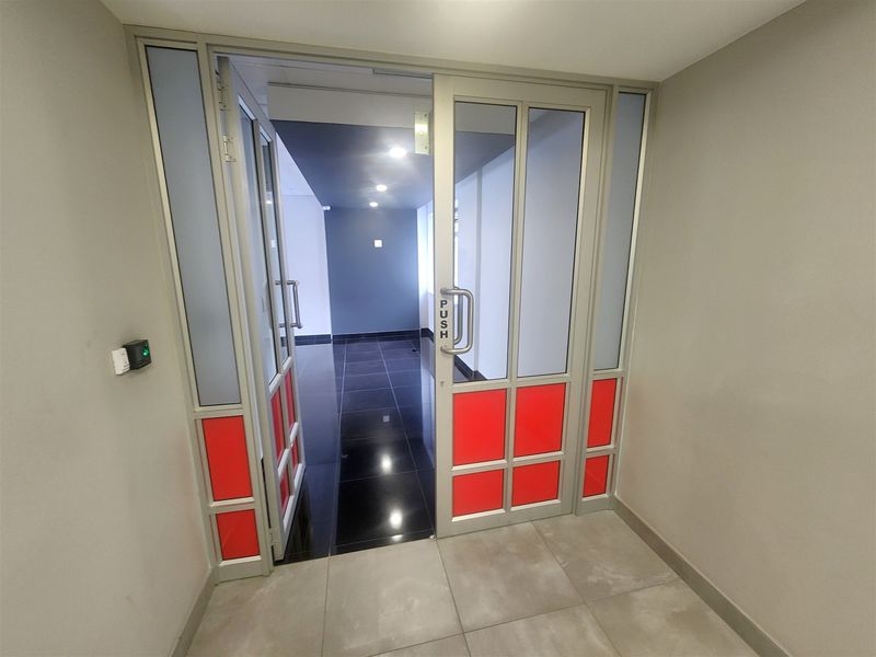 A modern office entrance featuring an aluminium framed glass door with access control, leading into a clean, tiled hallway with recessed lighting.