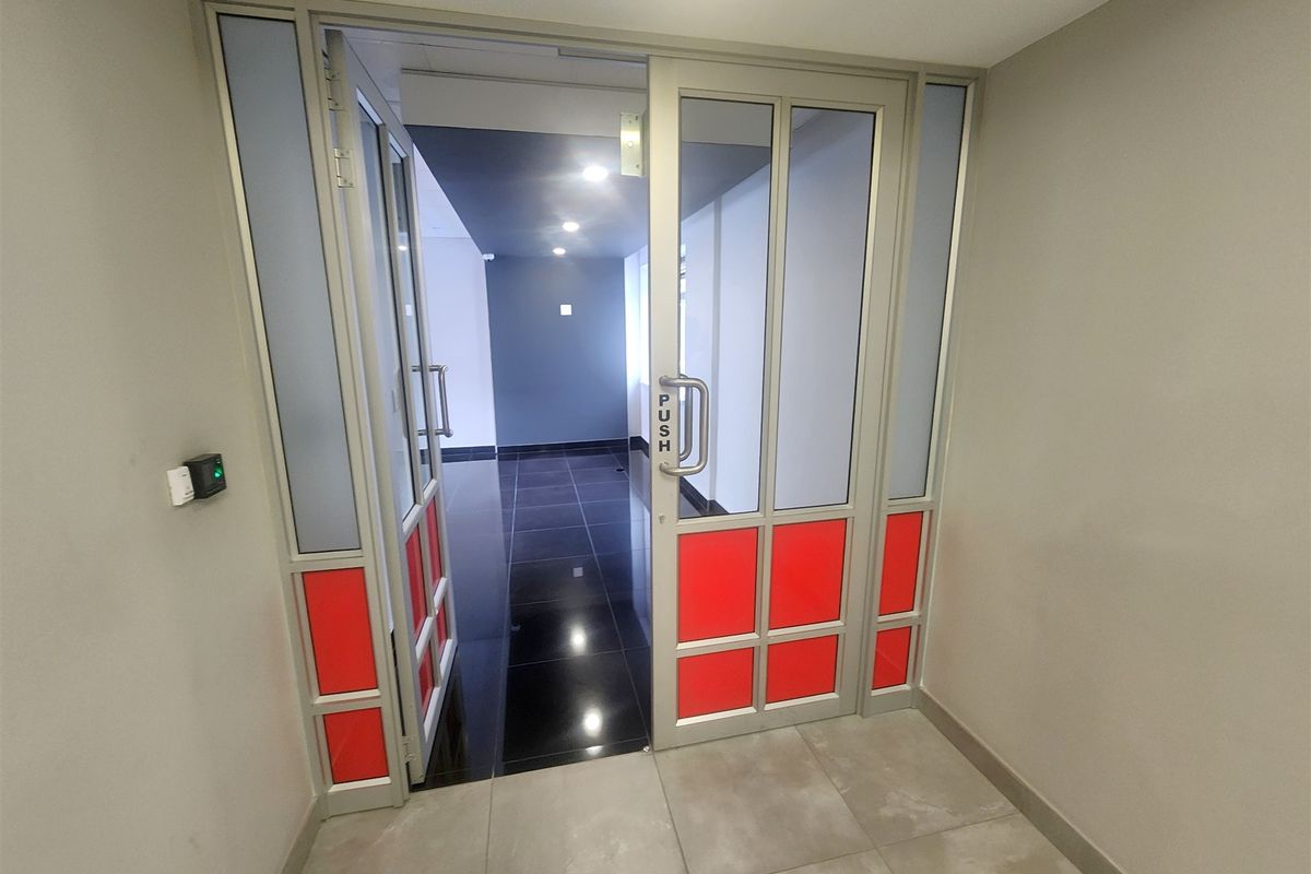 A modern office entrance featuring an aluminium framed glass door with access control, leading into a clean, tiled hallway with recessed lighting.