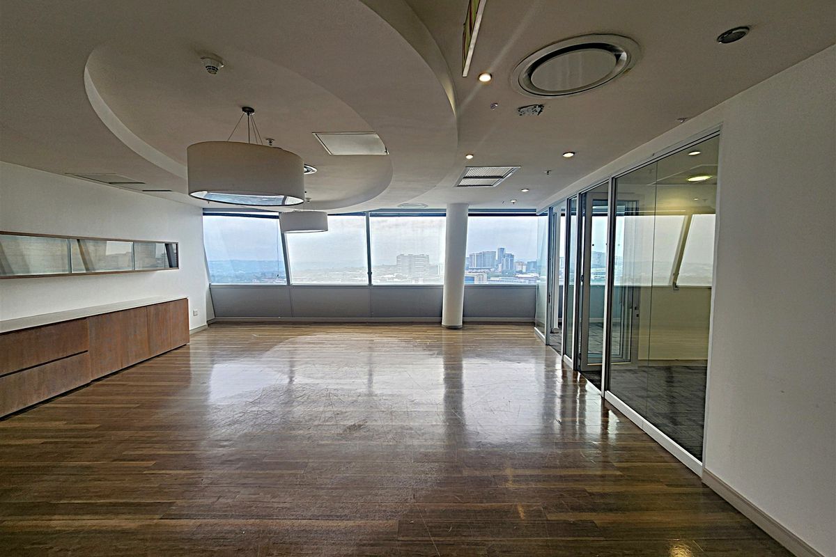 Spacious modern office area featuring hardwood flooring, floor-to-ceiling windows with city views, glass partitions, and integrated ceiling lighting.