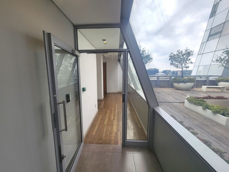 A modern office balcony featuring timber decking, built-in planters, and large glass sliding doors providing access to the outdoor terrace area.
