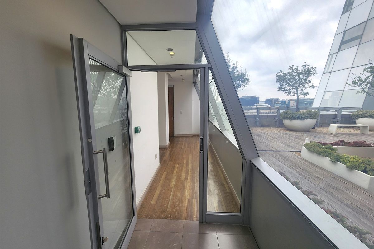A modern office balcony featuring timber decking, built-in planters, and large glass sliding doors providing access to the outdoor terrace area.