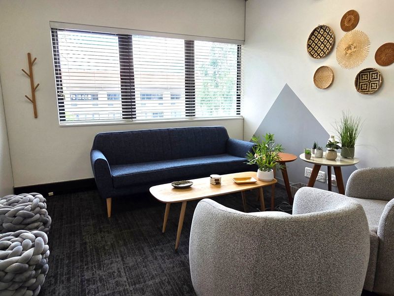 A well-maintained office space featuring carpeted flooring, large windows with venetian blinds, and integrated electrical outlets.