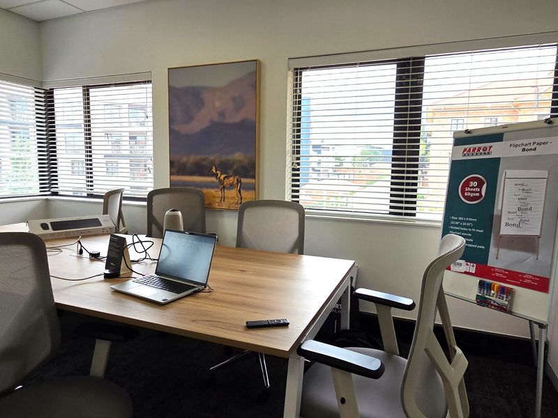 A professional office meeting room featuring large windows with venetian blinds, carpeted flooring, and a suspended ceiling.