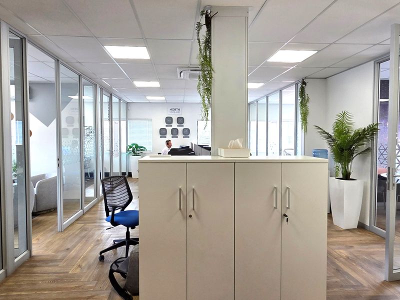 Modern office space featuring glass partition walls, suspended ceilings with recessed lighting, and durable laminate flooring, creating a bright and professional work environment.