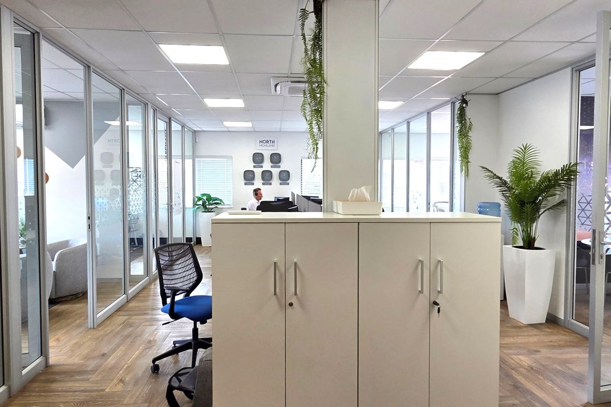 Modern office space featuring glass partition walls, suspended ceilings with recessed lighting, and durable laminate flooring, creating a bright and professional work environment.