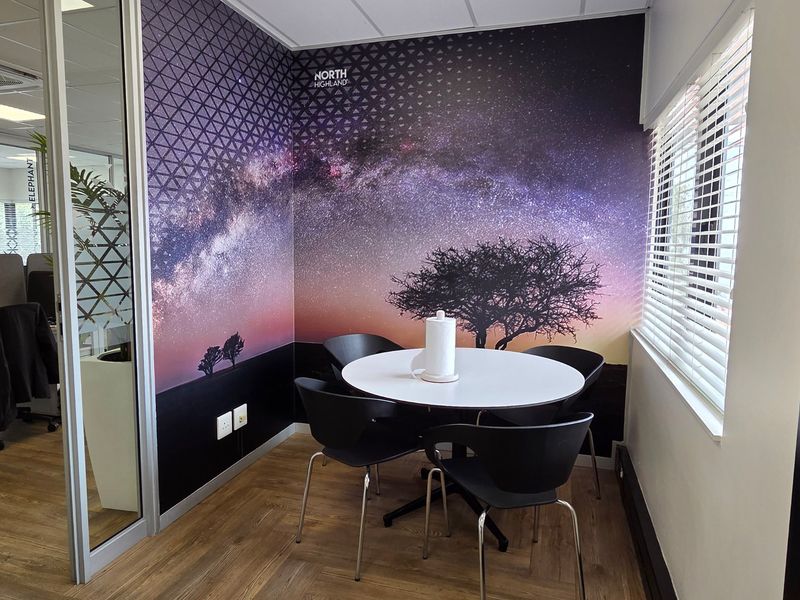 A modern office meeting nook featuring a decorative galaxy-themed feature wall, laminate flooring, and a glass partition wall.