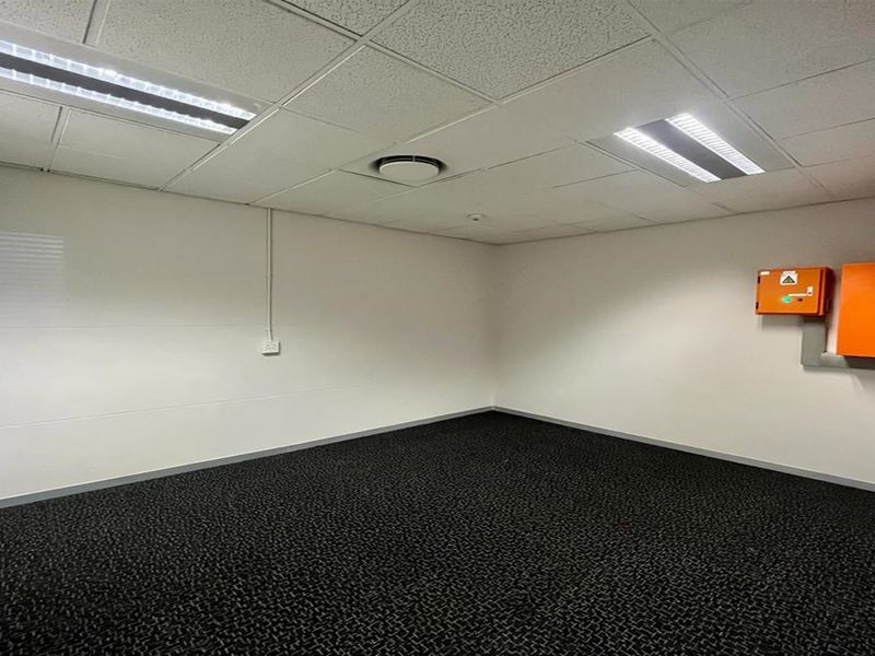 A clean, empty office space featuring a suspended ceiling with recessed lighting, dark carpeting, and wall-mounted electrical infrastructure.
