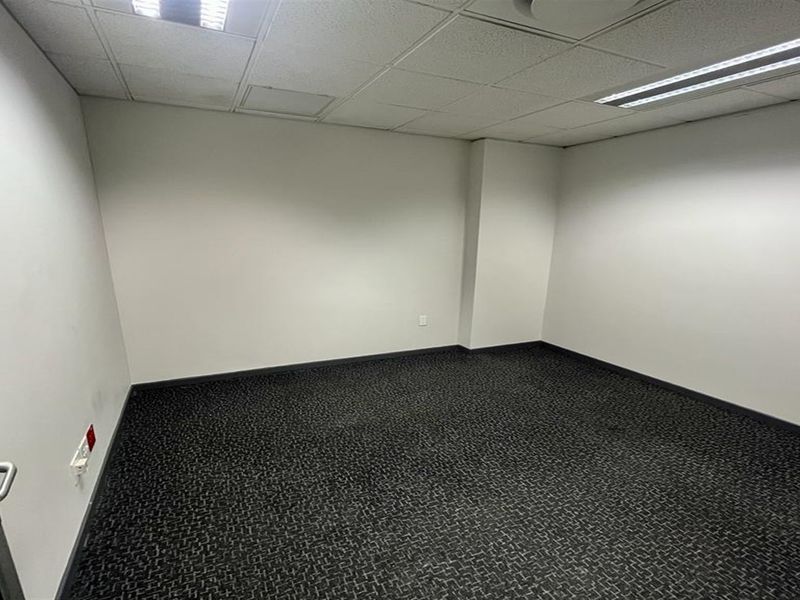 A clean, empty office space featuring neutral walls, carpeted flooring, and a suspended ceiling with recessed lighting.