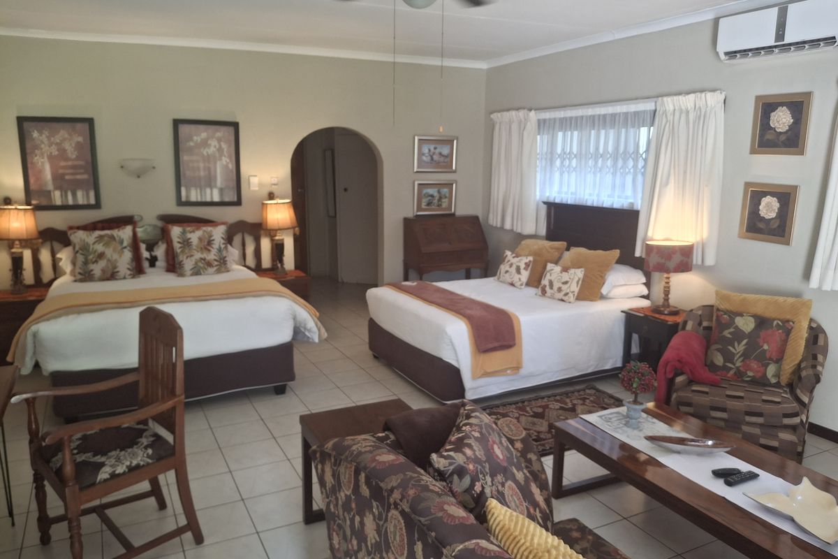 Spacious bedroom featuring tiled flooring, a ceiling fan, and a wall-mounted air conditioning unit, with an arched doorway leading to an adjoining area.