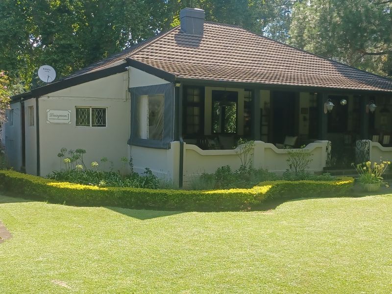 A well-maintained guest house exterior featuring a covered patio, tiled roof, and a neatly landscaped garden with a brick pathway.