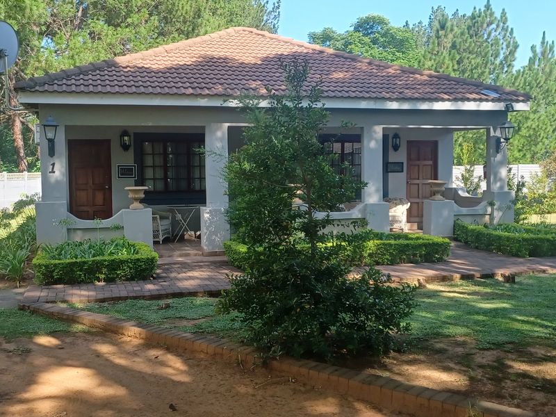 A well-maintained guest house unit featuring a covered patio, tiled roof, and established garden surroundings with brick-paved pathways.