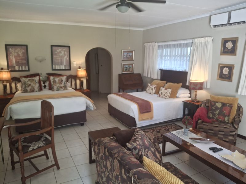 Spacious bedroom featuring tiled flooring, a ceiling fan, and a wall-mounted air conditioning unit, with an arched doorway leading to an adjoining area.
