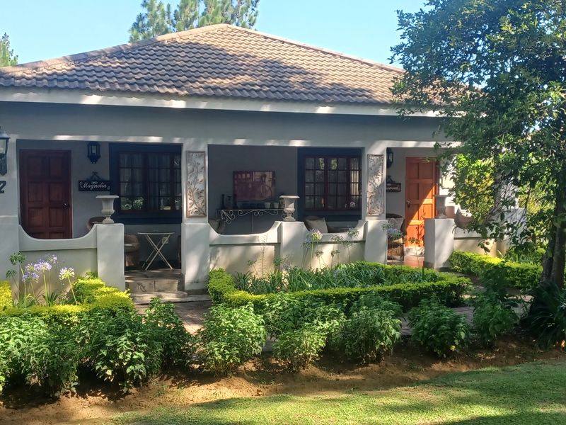 Front view of a guest house unit featuring a covered patio, tiled roof, and established garden surroundings.