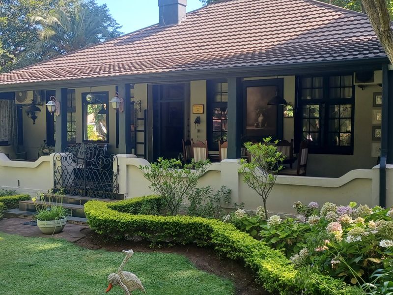 Charming guest house exterior featuring a covered veranda, tiled roof, and well-maintained landscaped garden with a masonry balustrade.