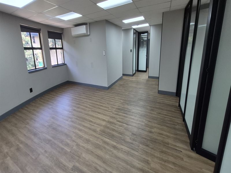 A modern, vacant office space featuring laminate flooring, suspended ceilings with recessed lighting, air conditioning, and sleek glass partition walls.