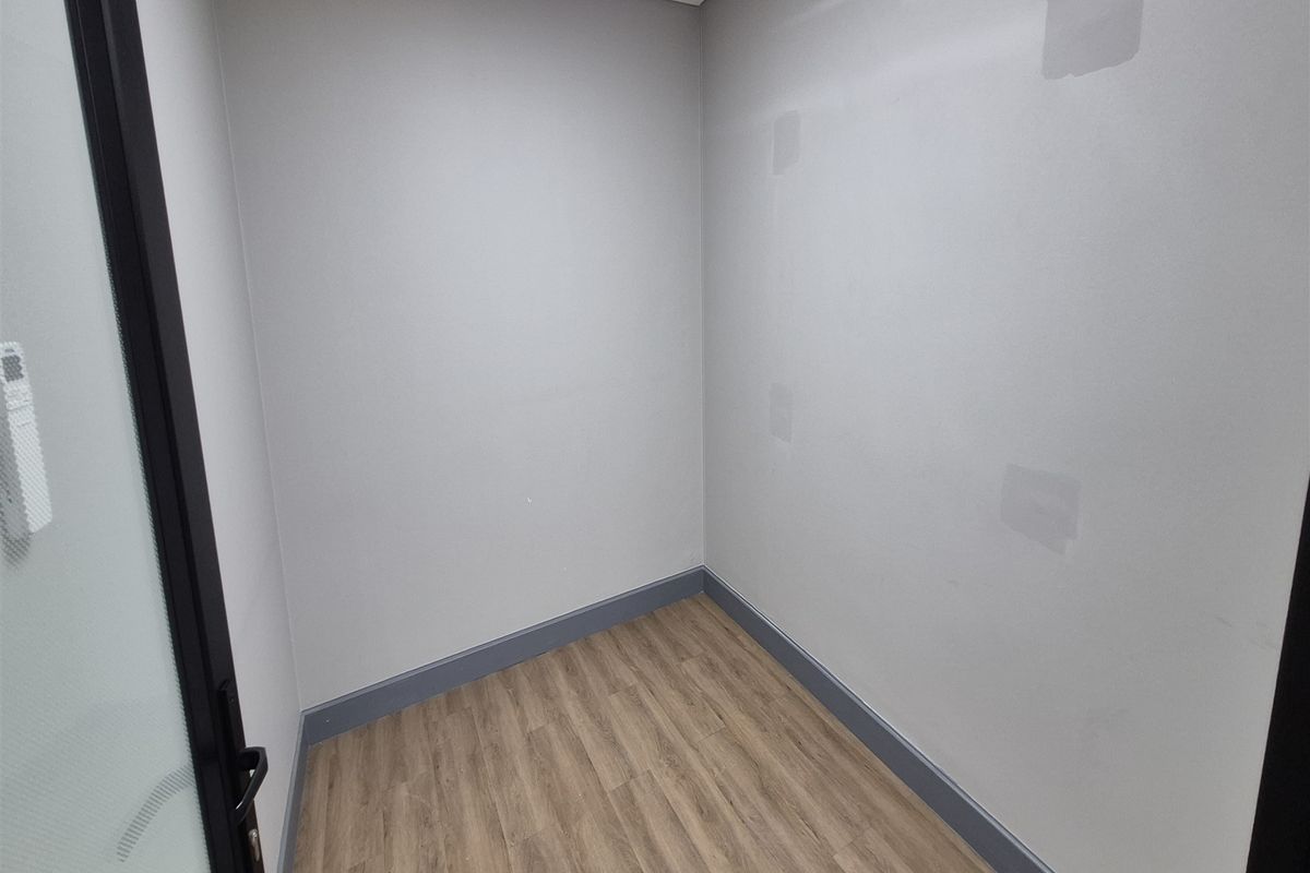 A vacant office space featuring laminate flooring, grey skirting boards, and a modern glass-panelled door, ready for custom fit-out.