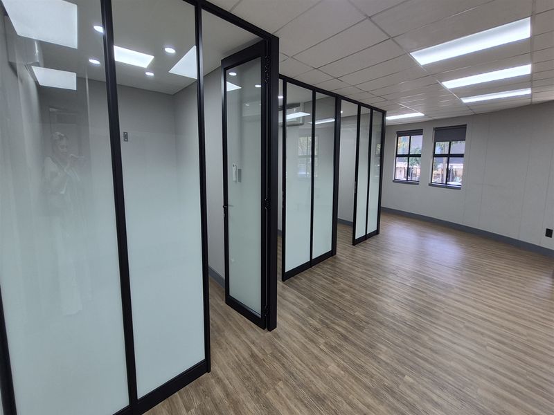 Modern office space featuring glass partition walls, suspended ceilings with recessed lighting, and durable laminate flooring in a clean, professional environment.
